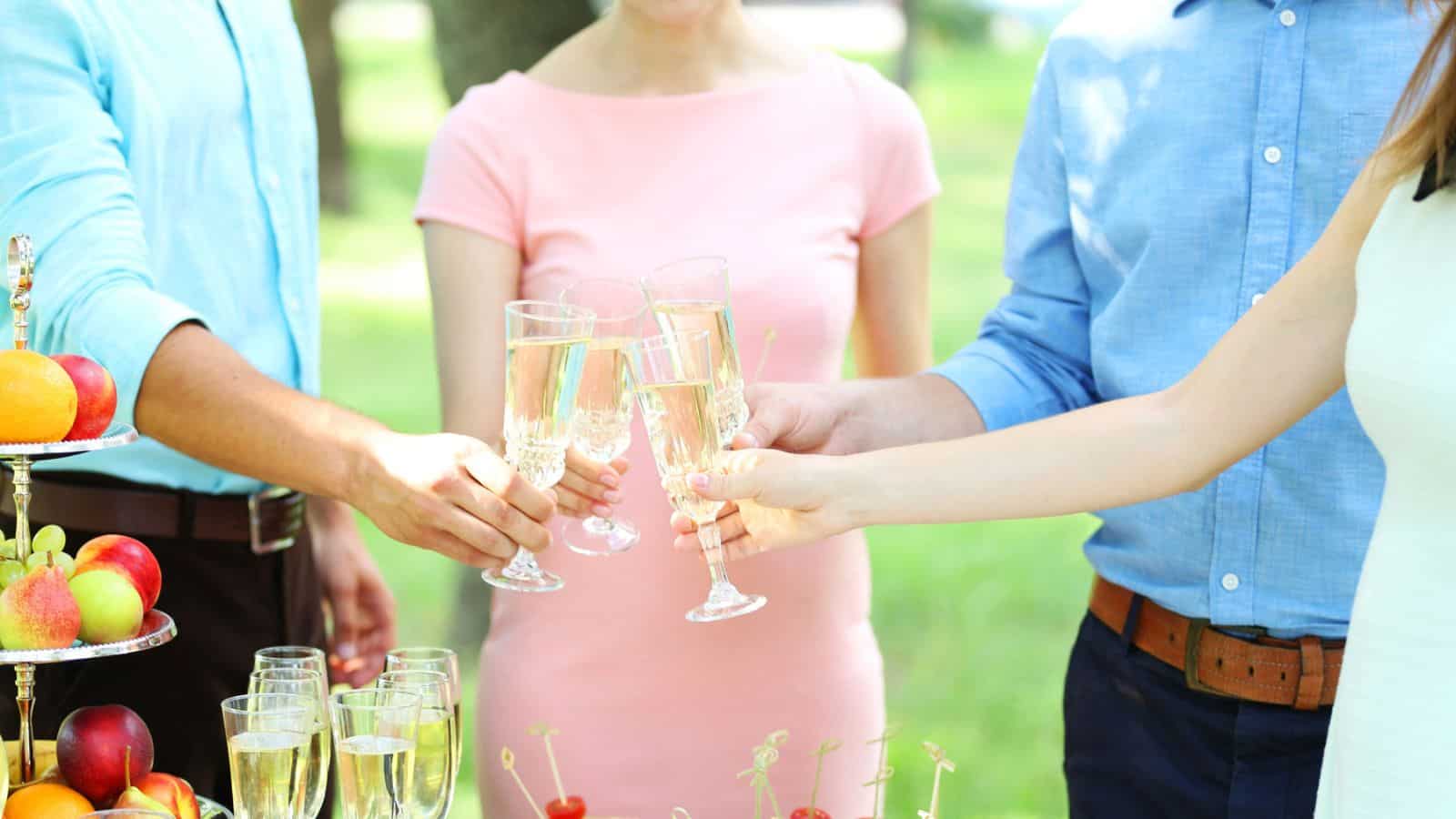 Four people clinking champagne glasses at an outdoor gathering with fruit on a table.