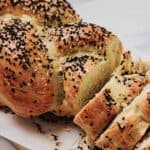 A close-up of Easy Challah bread, sliced and topped with sesame and black seeds, resting on parchment paper.