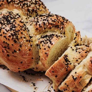 A close-up of Easy Challah bread, sliced and topped with sesame and black seeds, resting on parchment paper.
