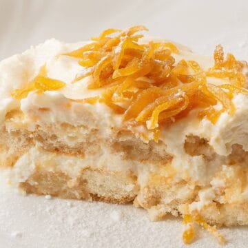A slice of creamy tiramisu topped with shredded orange zest on a white plate.