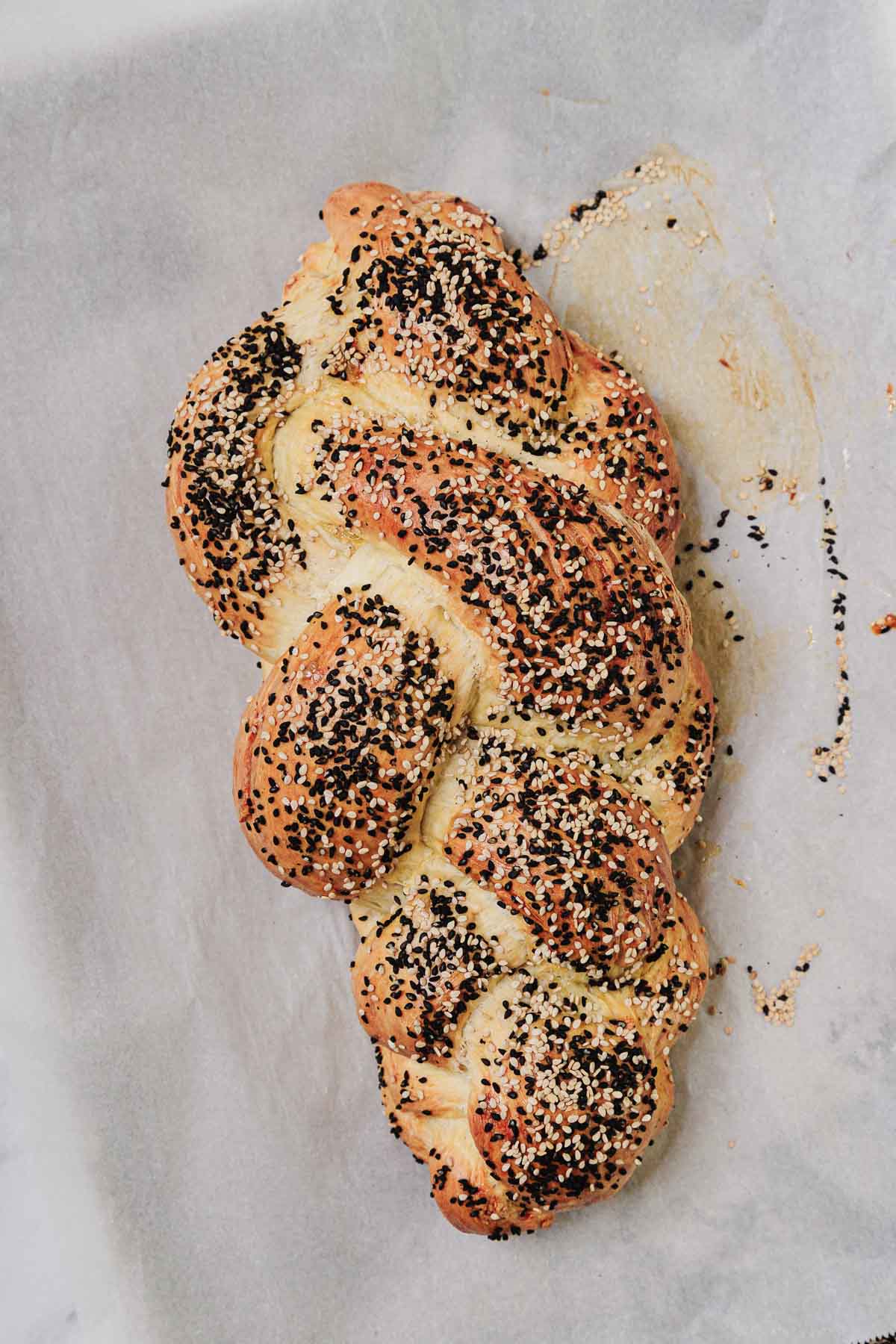 An easy challah braided loaf, topped with sesame and poppy seeds, rests beautifully on parchment paper.