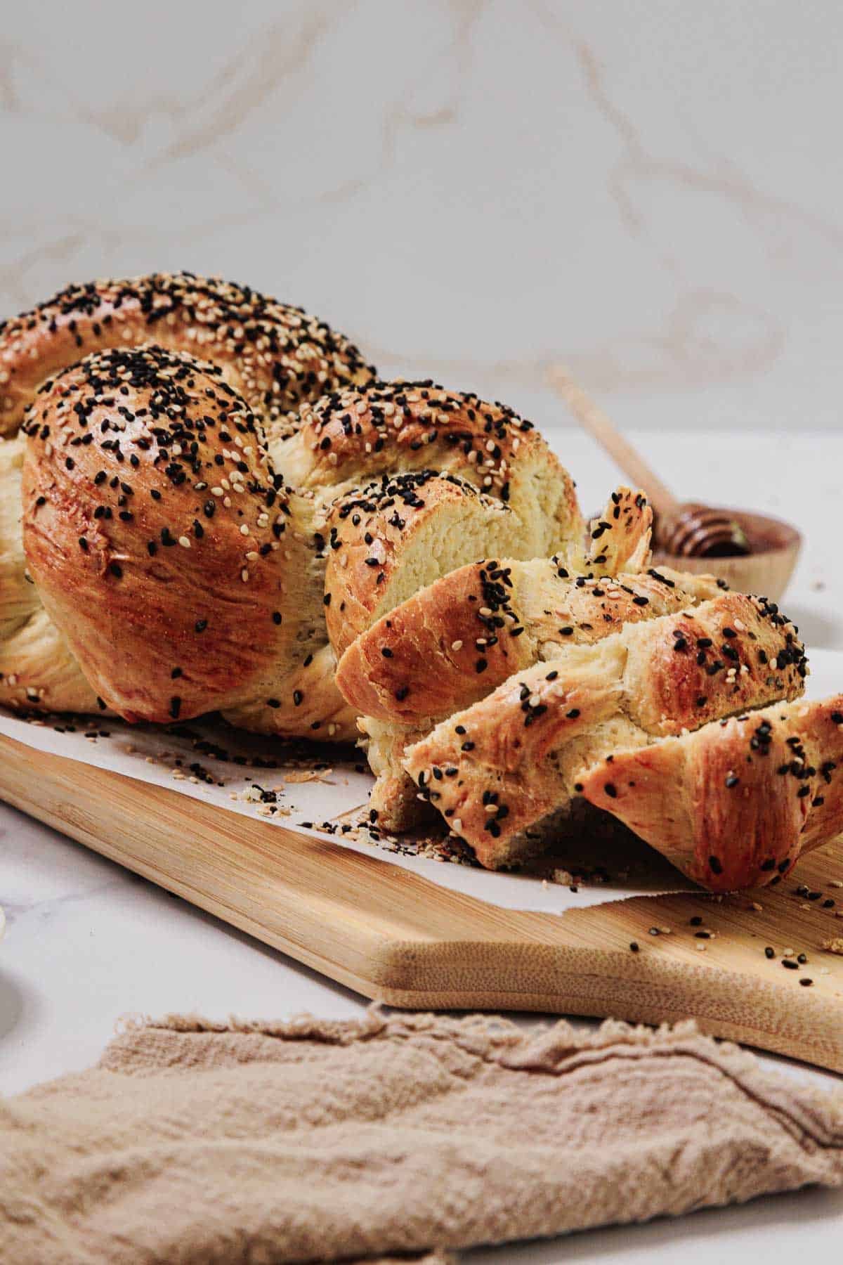 A sliced loaf of Easy Challah, beautifully braided and topped with black sesame seeds, rests on a wooden cutting board.