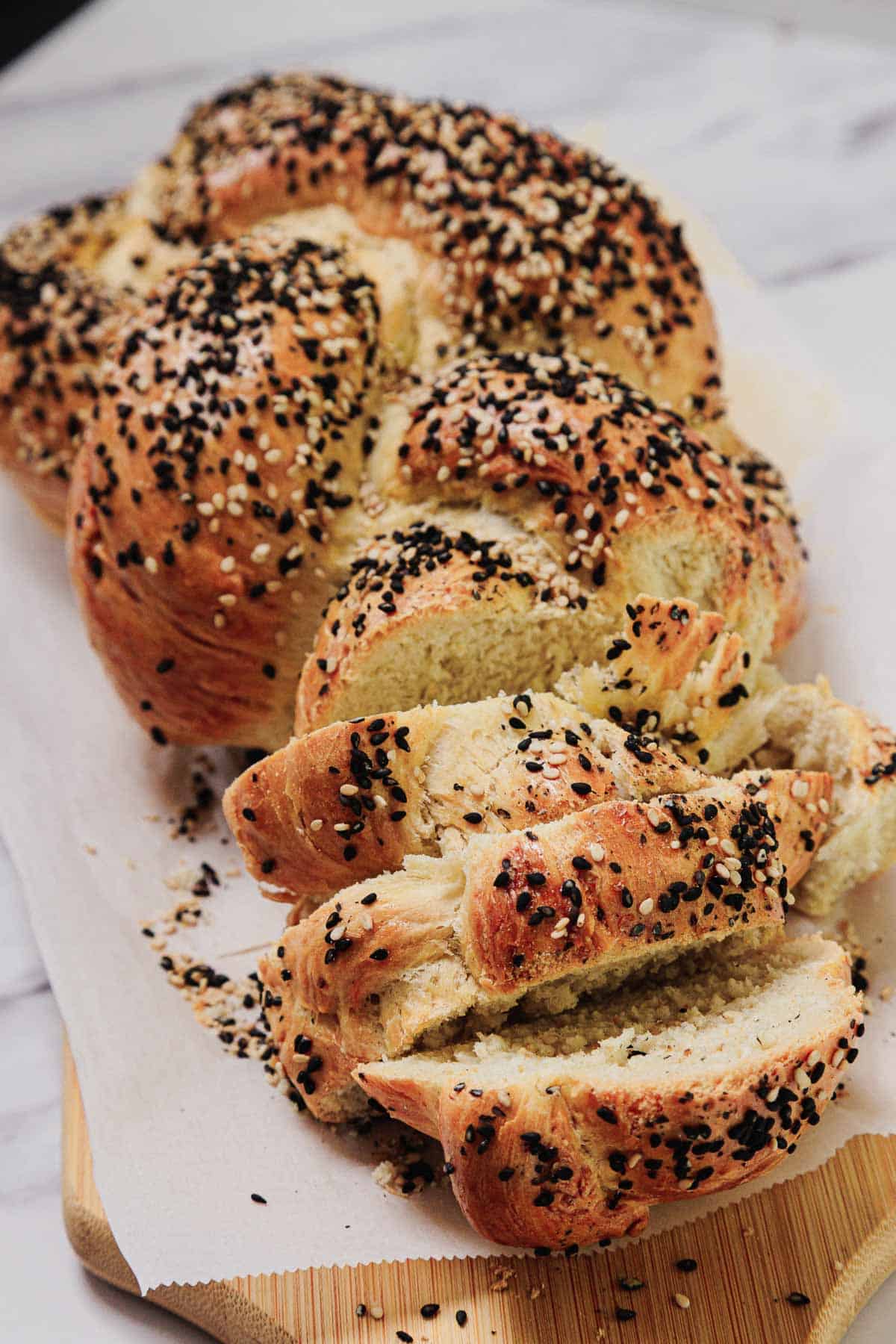 Easy Challah sliced and topped with sesame and black seeds rests on parchment paper.