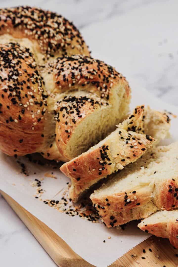 Easy Challah sliced and topped with black and white sesame seeds, presented on parchment paper.