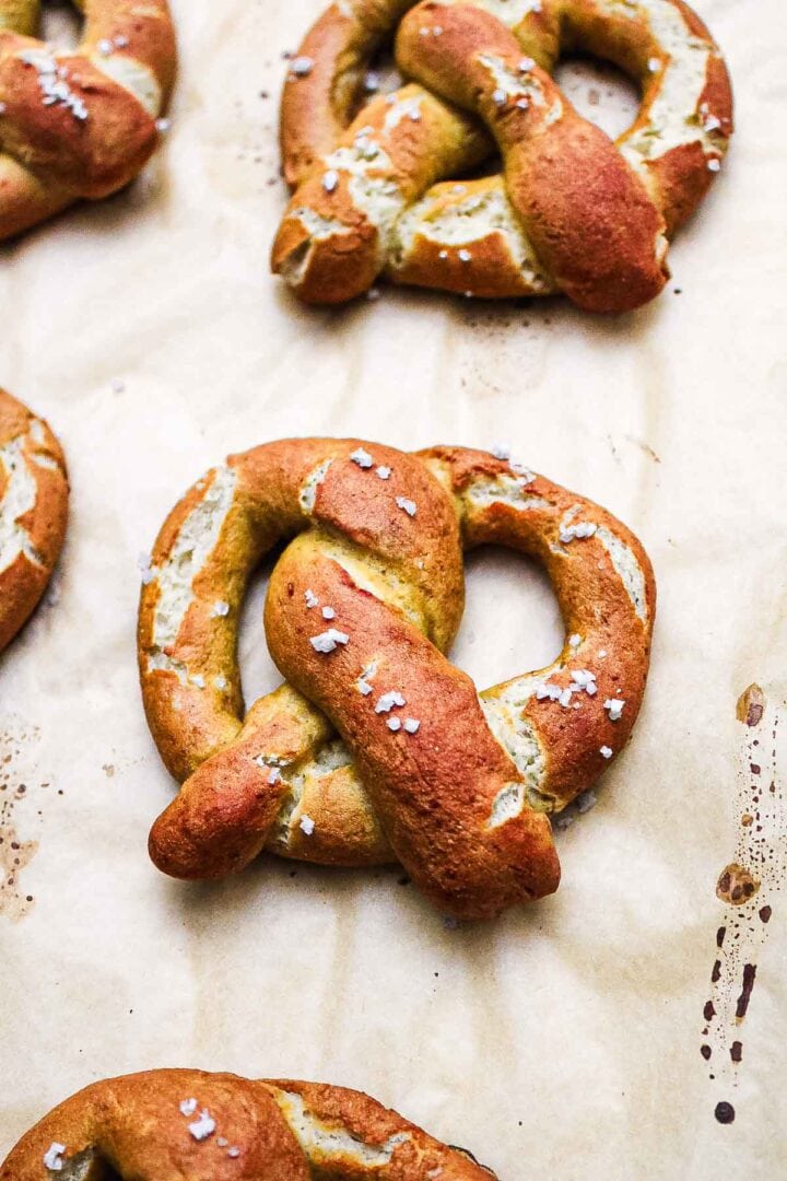 Freshly baked Gluten-Free Soft Pretzels topped with coarse salt on parchment paper.