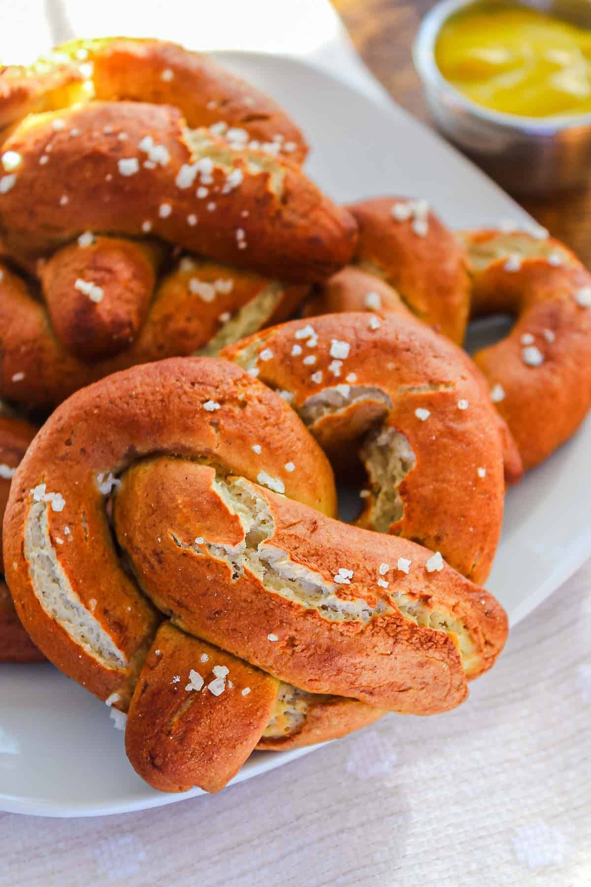 Close-up of Gluten-Free Soft Pretzels with coarse salt on a white plate, with a small dish of mustard in the background.