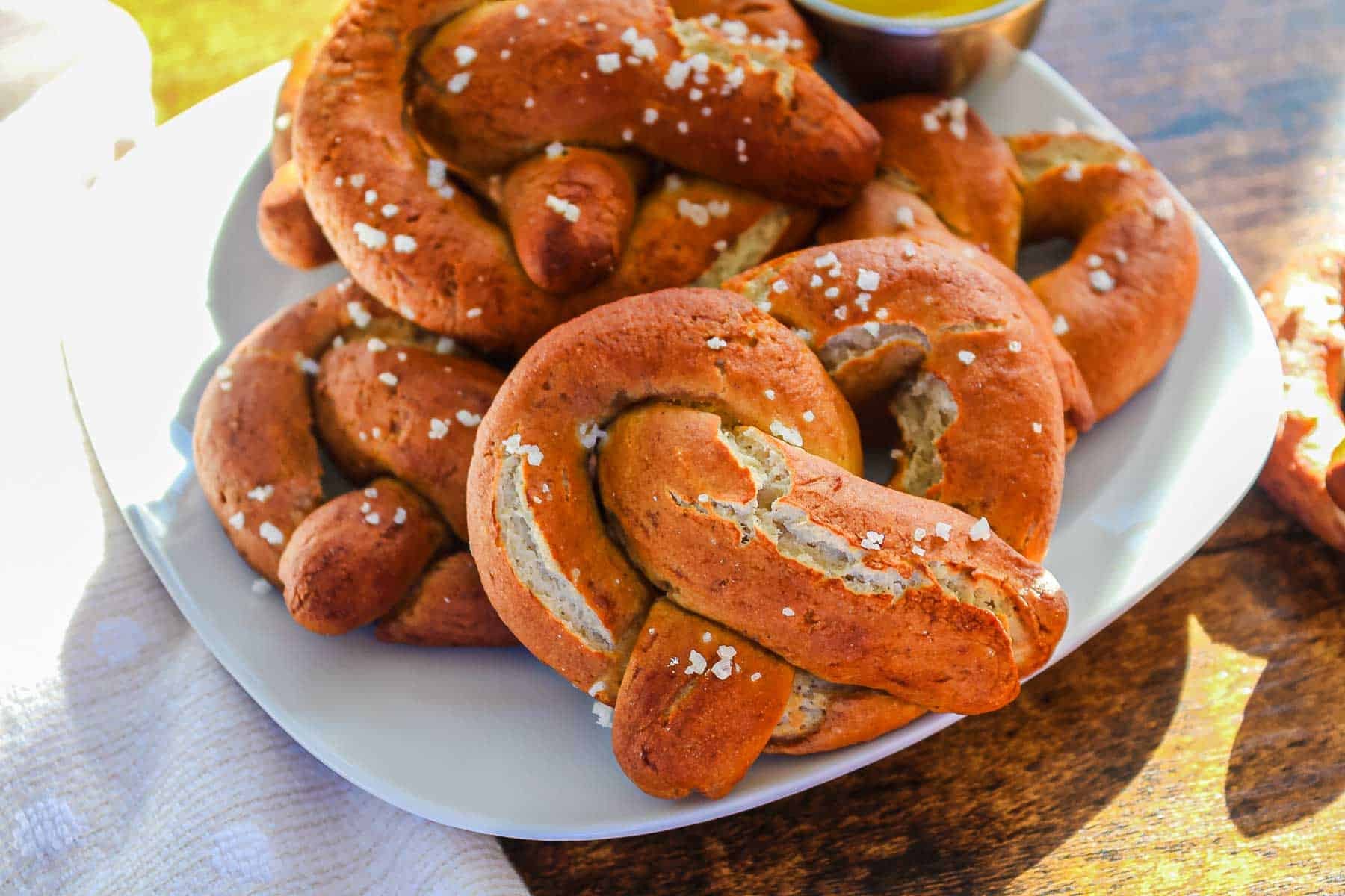 Plate of gluten-free soft pretzels topped with coarse salt, served on a white dish on a wooden table.