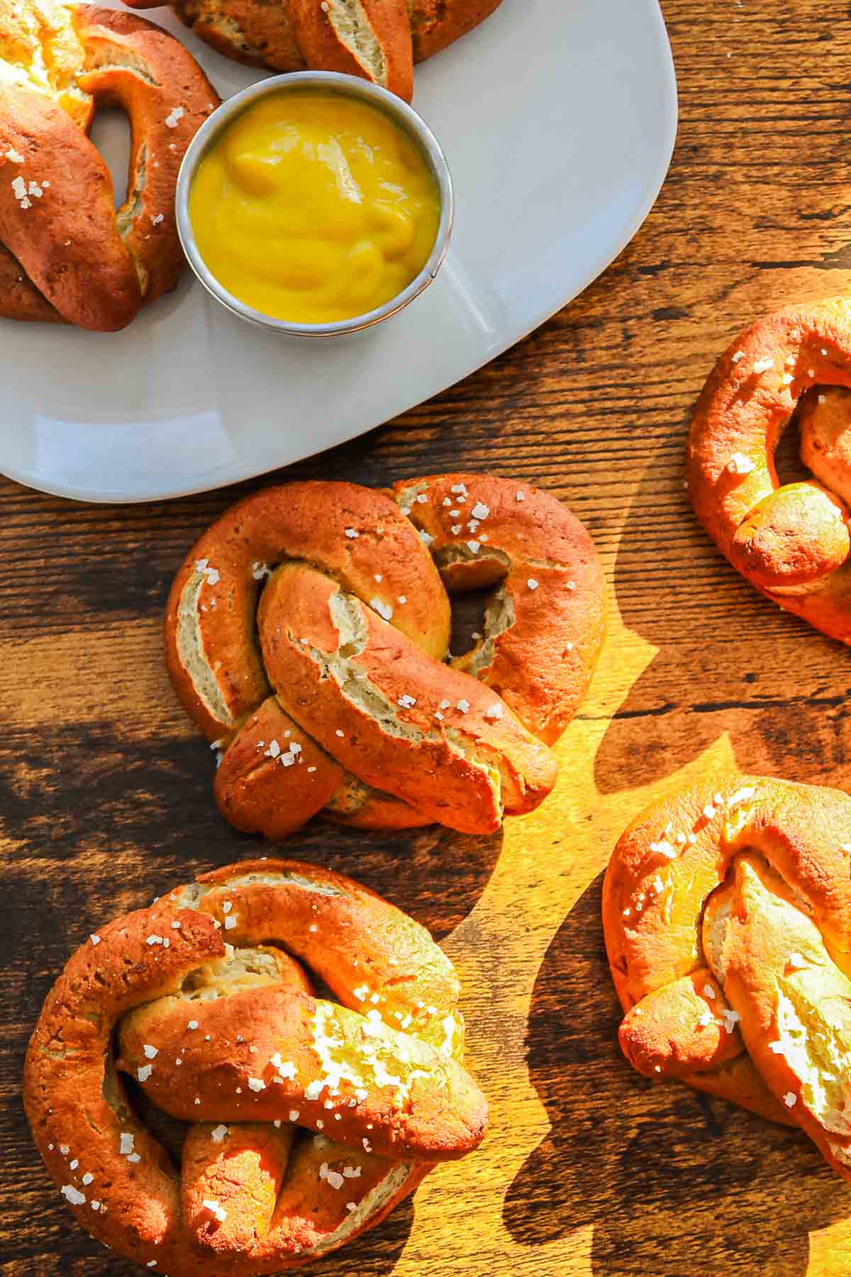 Gluten-Free Soft Pretzels sprinkled with salt on a wooden table, served with a cup of yellow mustard sauce.