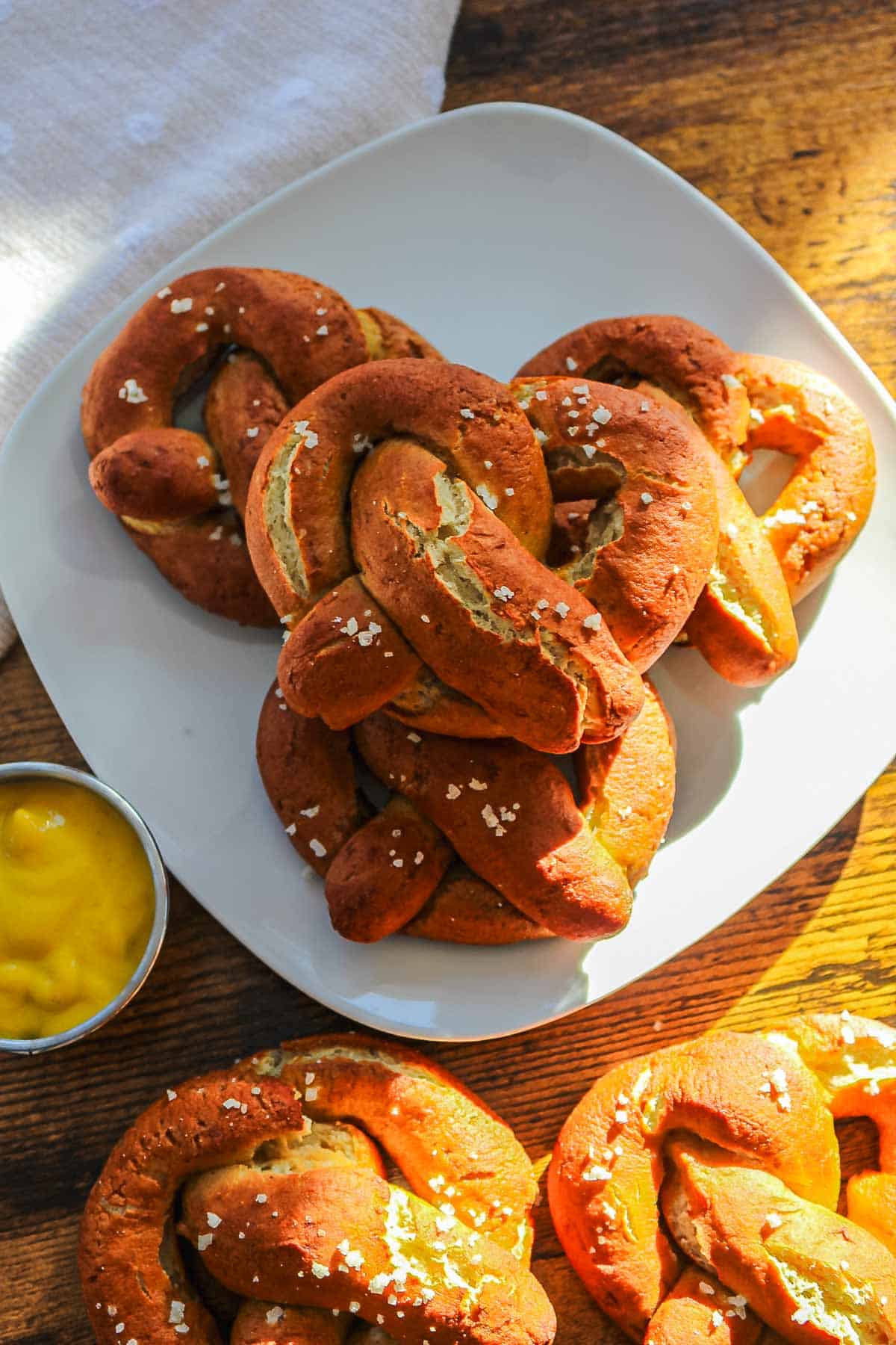 A plate of gluten-free soft pretzels with coarse salt, served with a small cup of yellow mustard on a wooden table.