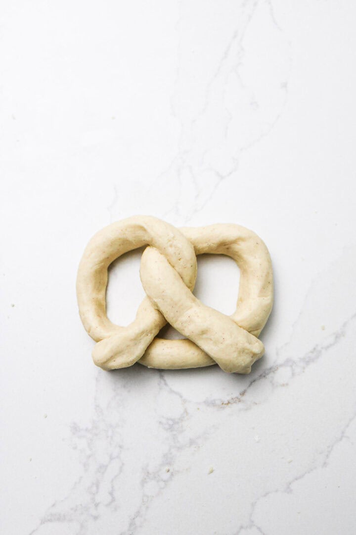 A raw, twisted Gluten-Free Soft Pretzels dough sits on a white marble surface.