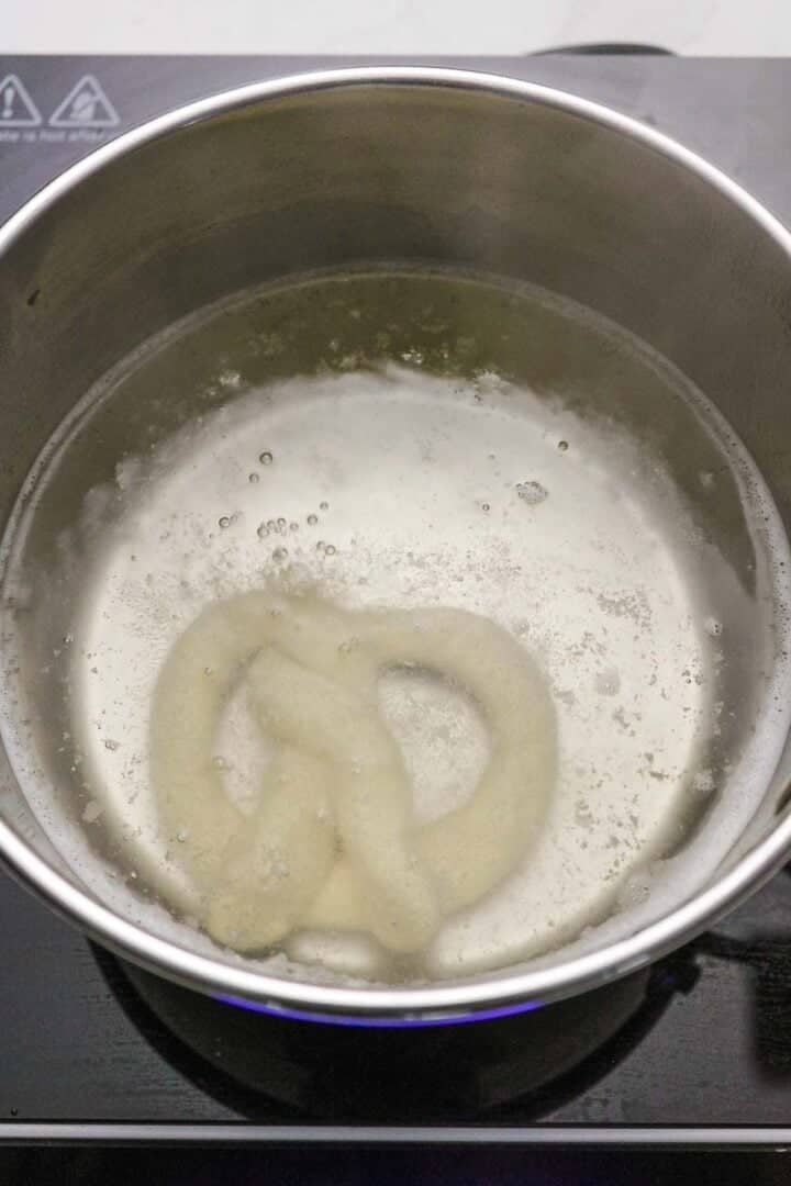 A gluten-free soft pretzel is boiling in a pot of water on the stovetop, ready for baking into a delicious, chewy snack.