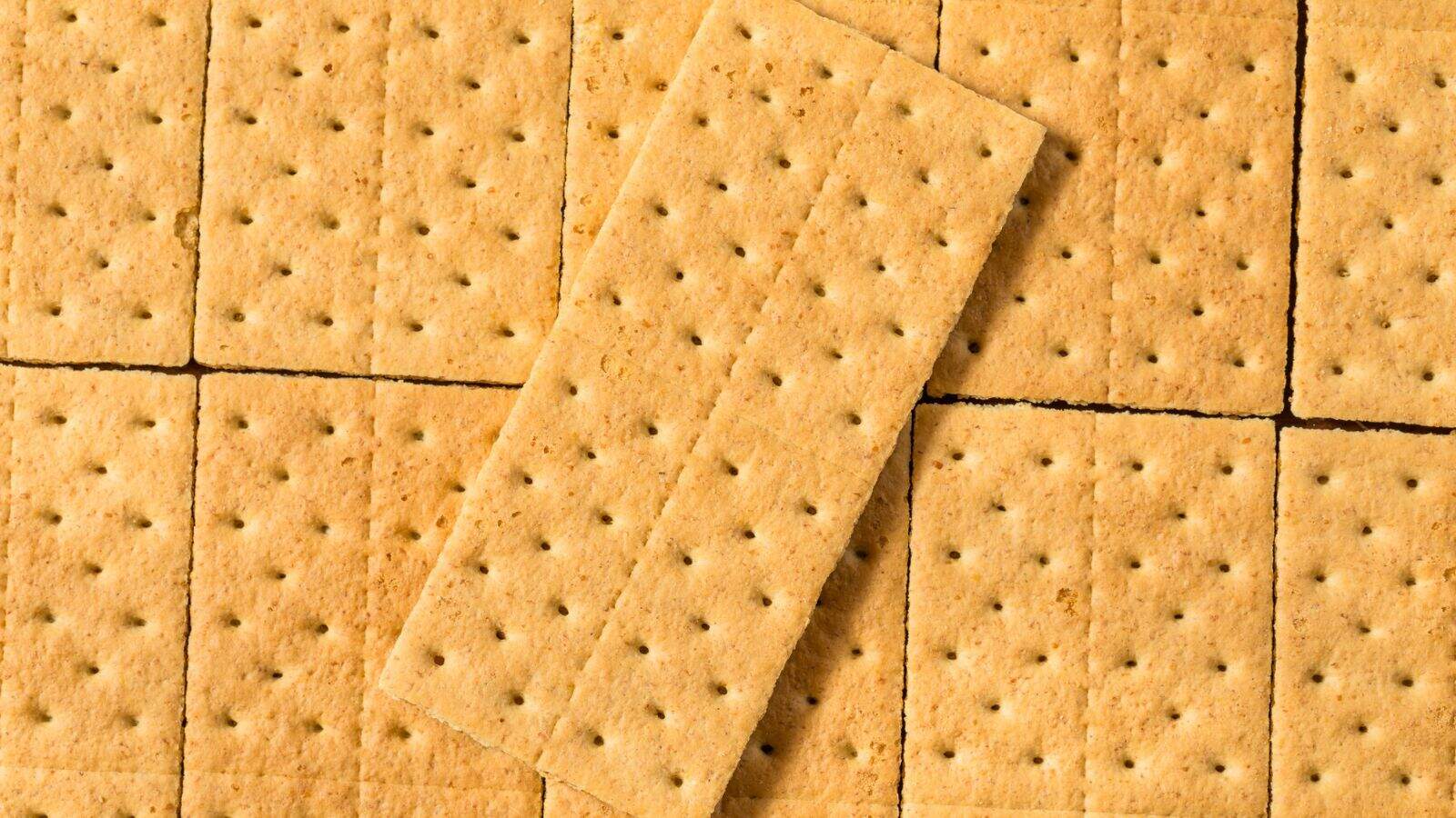A group of rectangular graham crackers arranged in a grid pattern with one cracker placed diagonally on top of the others. Each cracker is light brown with small holes evenly spaced across the surface.