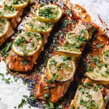 Harissa Salmon fillets baked with lemon slices and chopped herbs on parchment paper.