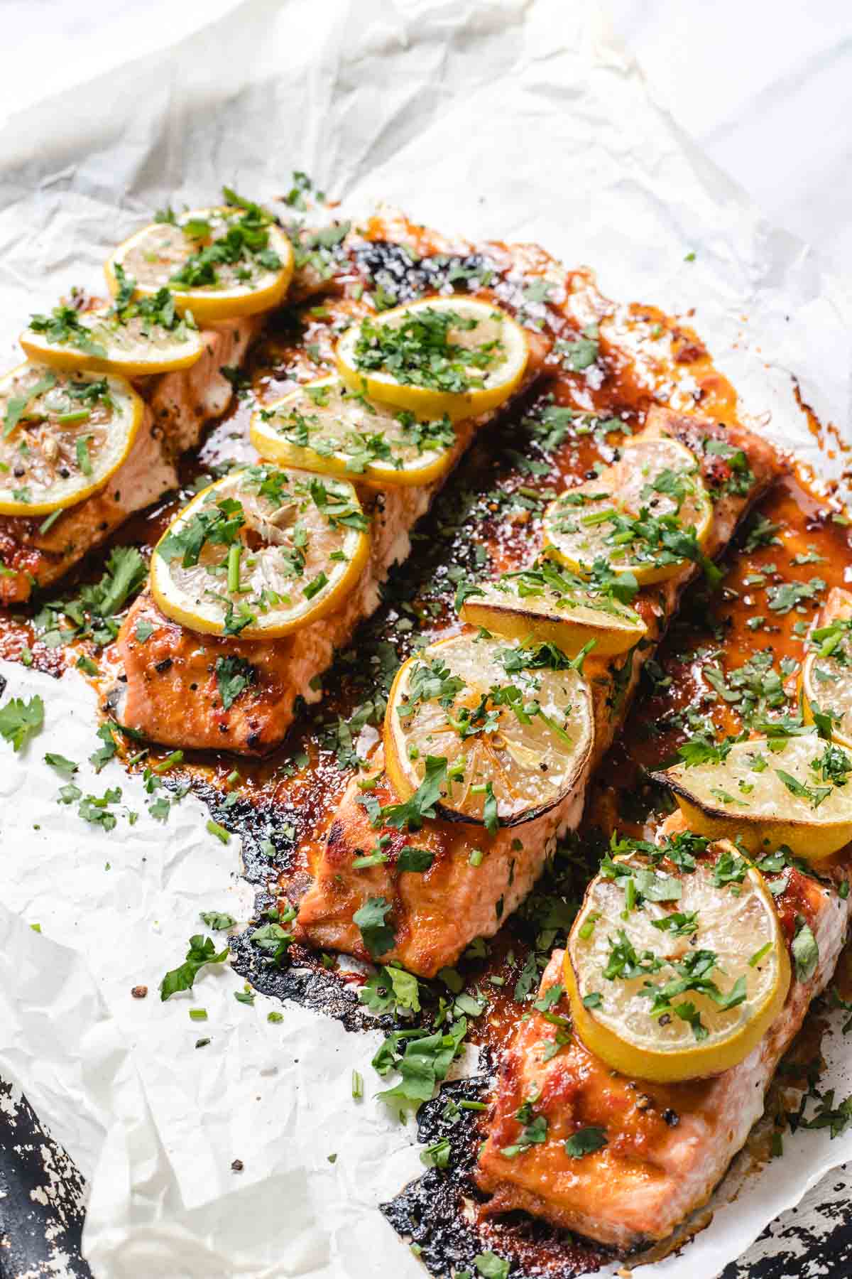 Baked salmon fillets topped with lemon slices and fresh herbs on parchment paper.