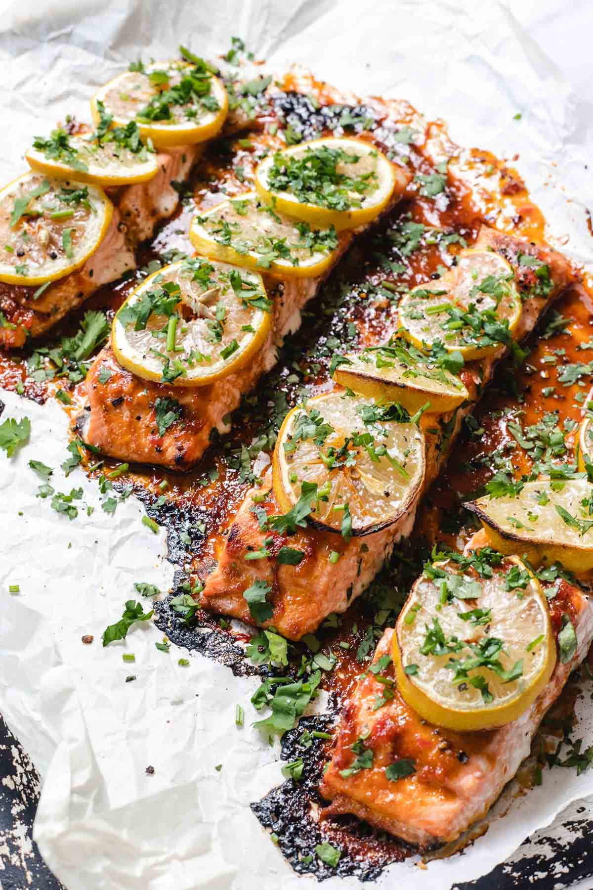 Baked salmon fillets topped with lemon slices and chopped herbs on parchment paper.