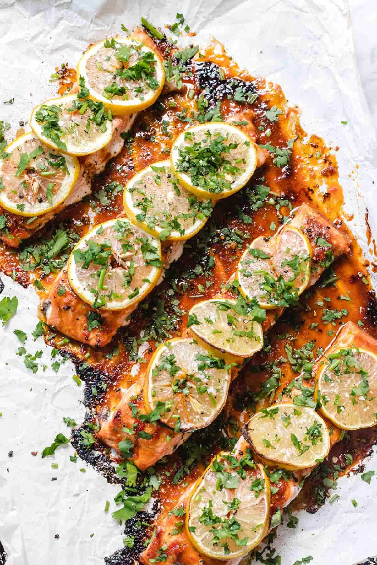 Baked salmon fillets topped with lemon slices and chopped herbs on parchment paper.