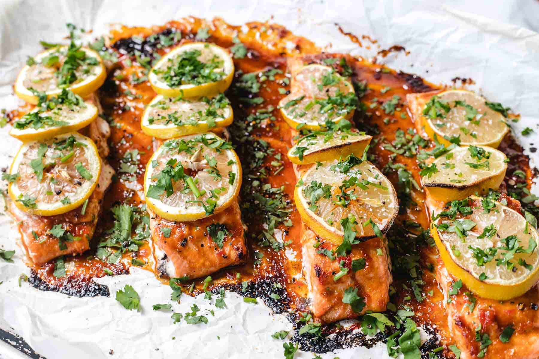 Baked salmon fillets topped with lemon slices and chopped herbs on a foil-lined baking sheet.