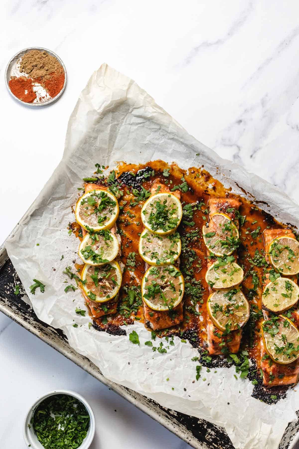 Baked salmon fillets topped with lemon slices and chopped herbs on parchment paper.