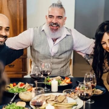 Group of friends smiling and enjoying dinner together at a table with wine and food.