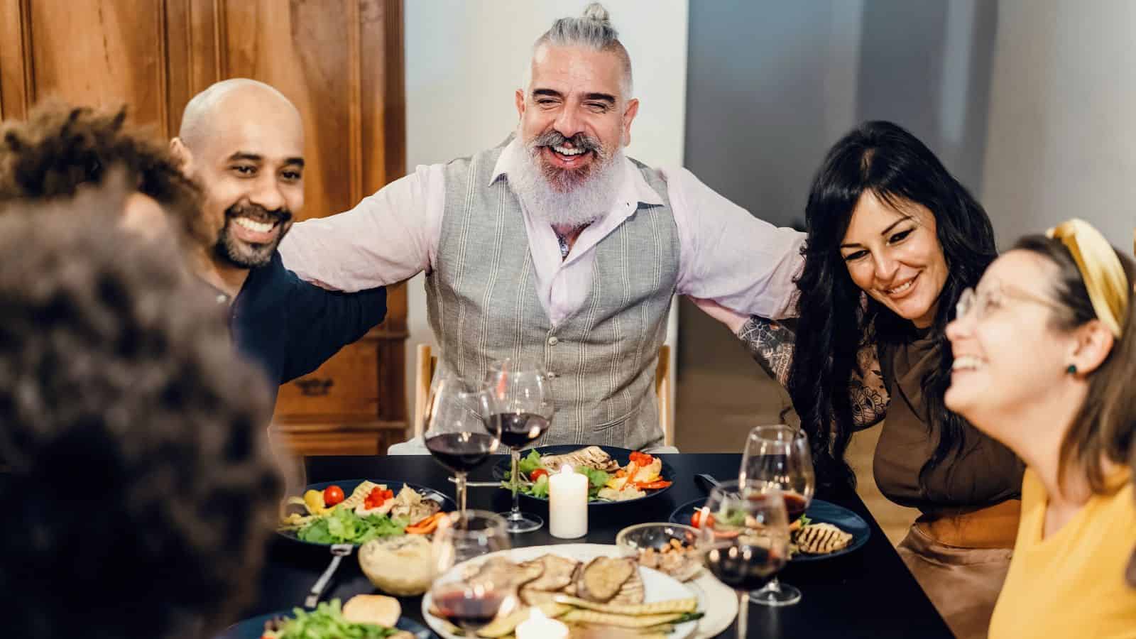 Group of friends smiling and enjoying dinner together at a table with wine and food.