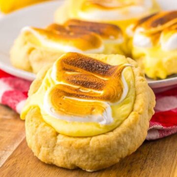 Close-up of lemon meringue cookies on a wooden board, with more cookies on a plate in the background.