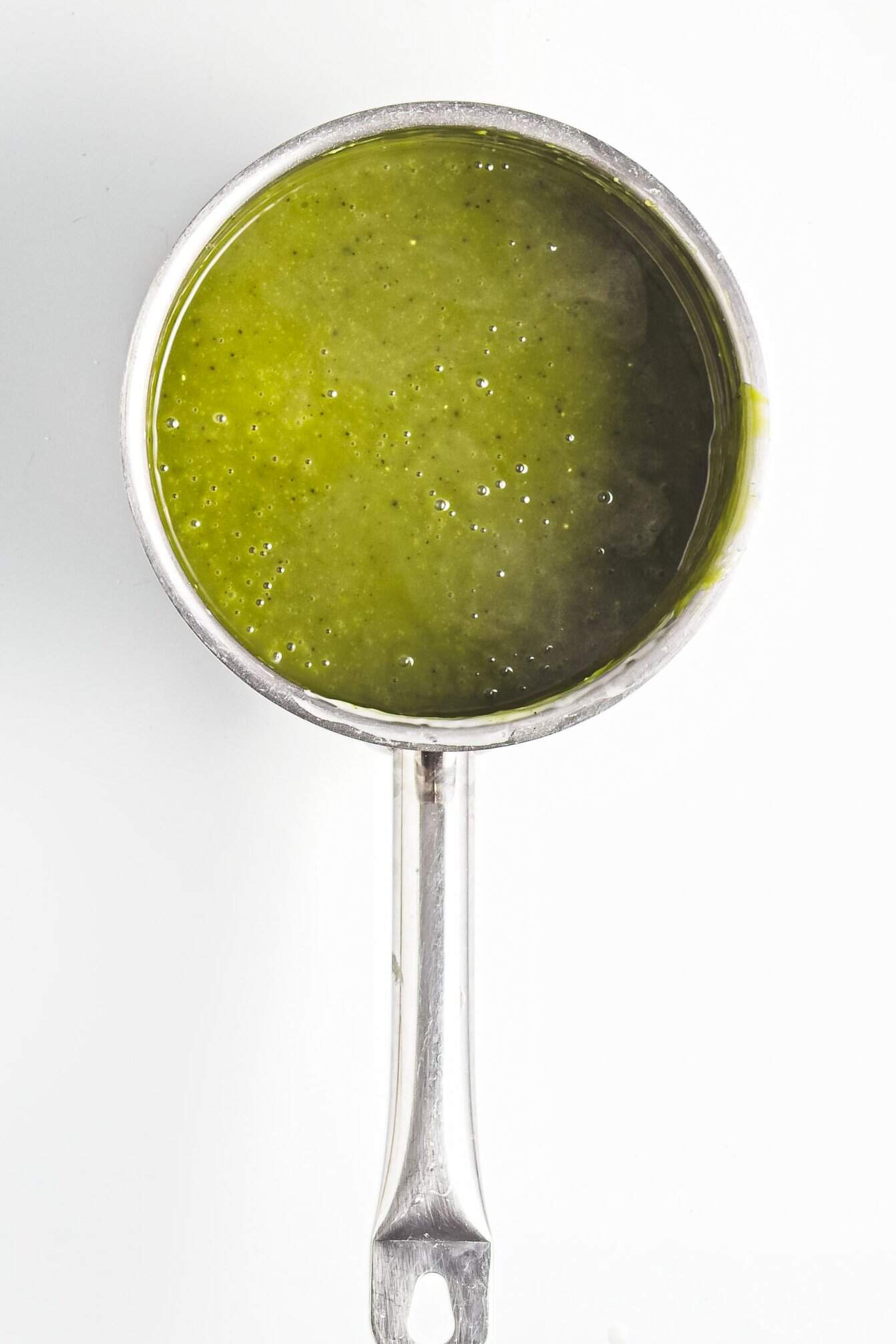 A metal saucepan filled with green sauce, viewed from above on a white background.