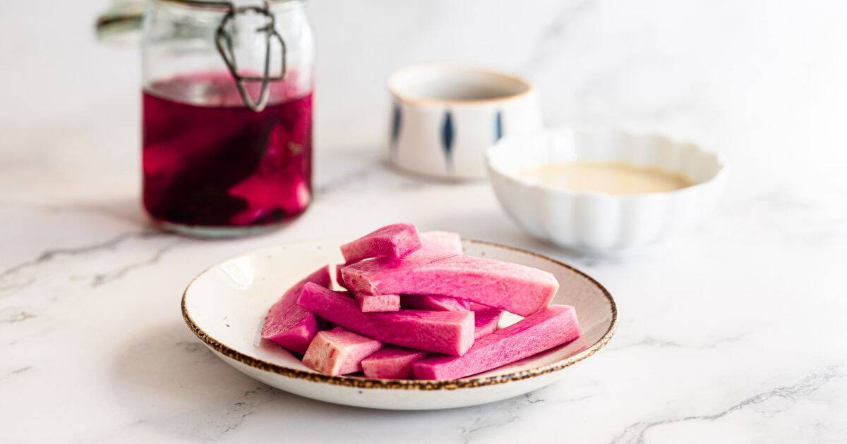 A plate of pink Middle Eastern Pickled Turnips sticks with sauces and a jar of vibrant pink liquid in the background.