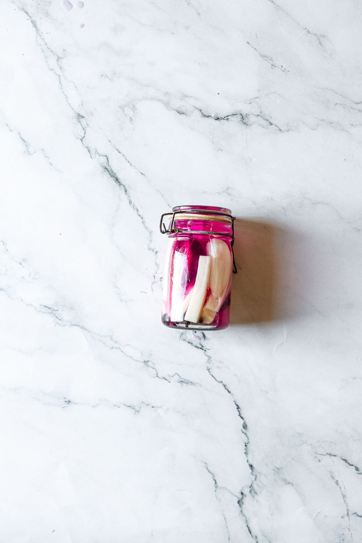 A glass jar of pickled radishes and Middle Eastern Pickled Turnips on a white marble surface.