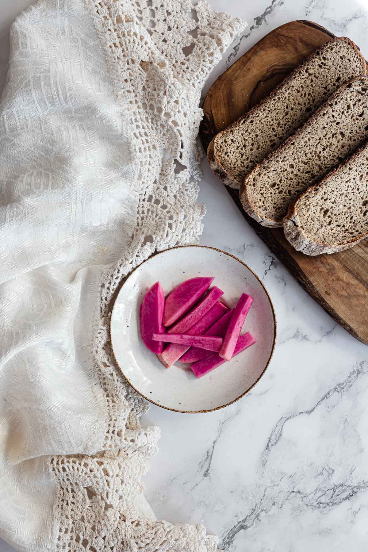 Sliced Middle Eastern Pickled Turnips on a plate beside three pieces of bread on a wooden board.
