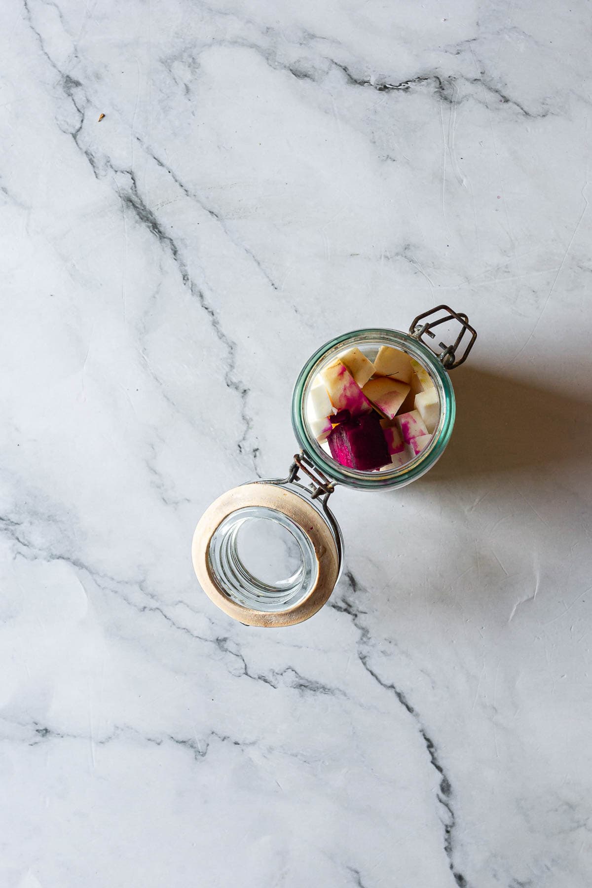 Open glass jar of Middle Eastern Pickled Turnips with chopped red and white vegetables on a marble surface, viewed from above.