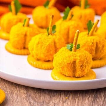 Mini pumpkin-shaped cheese balls on crackers with pretzel stems.