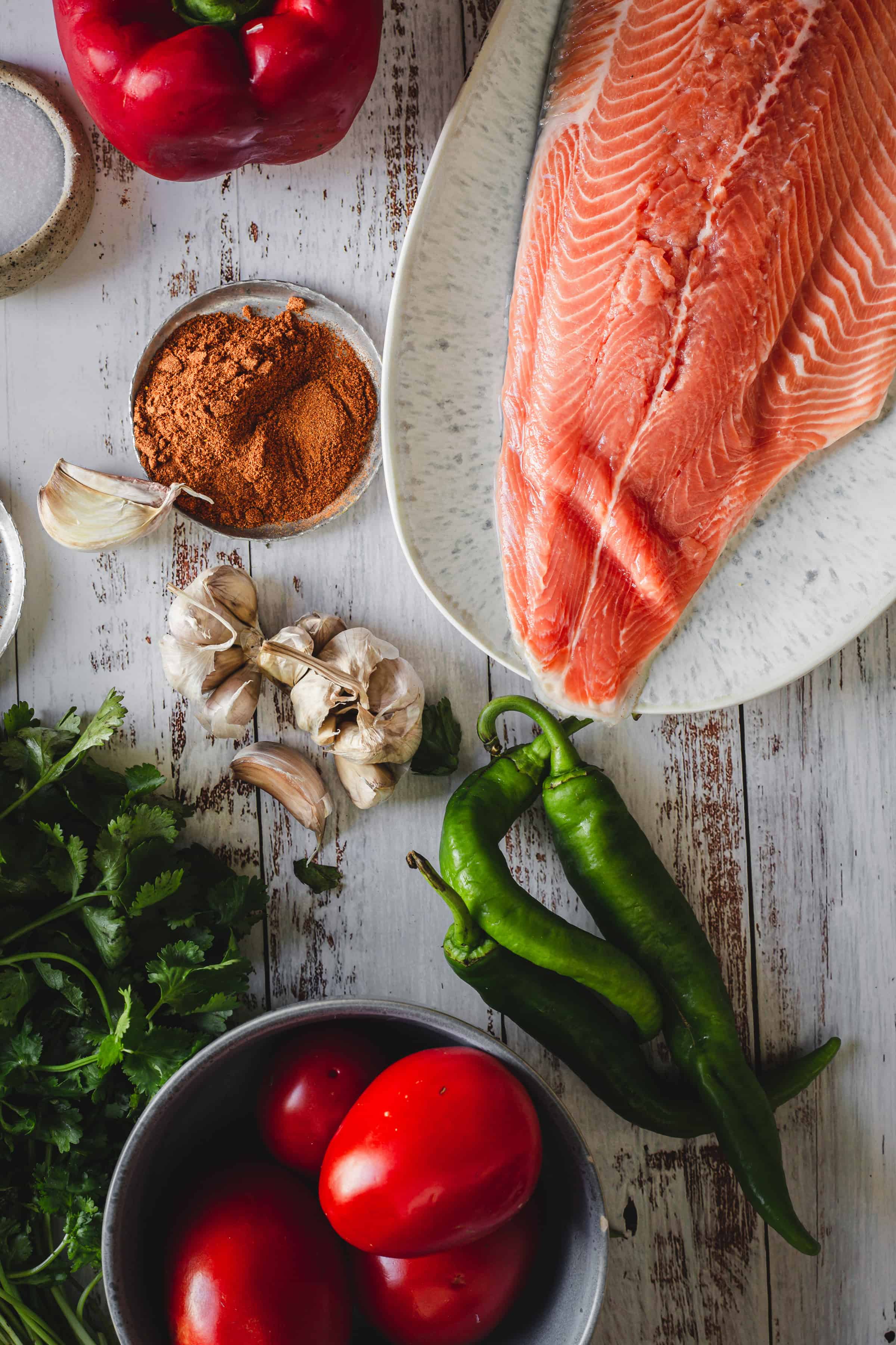 Moroccan salmon fillet, tomatoes, green chilies, bell pepper, garlic, cilantro, and spices displayed on a rustic table.