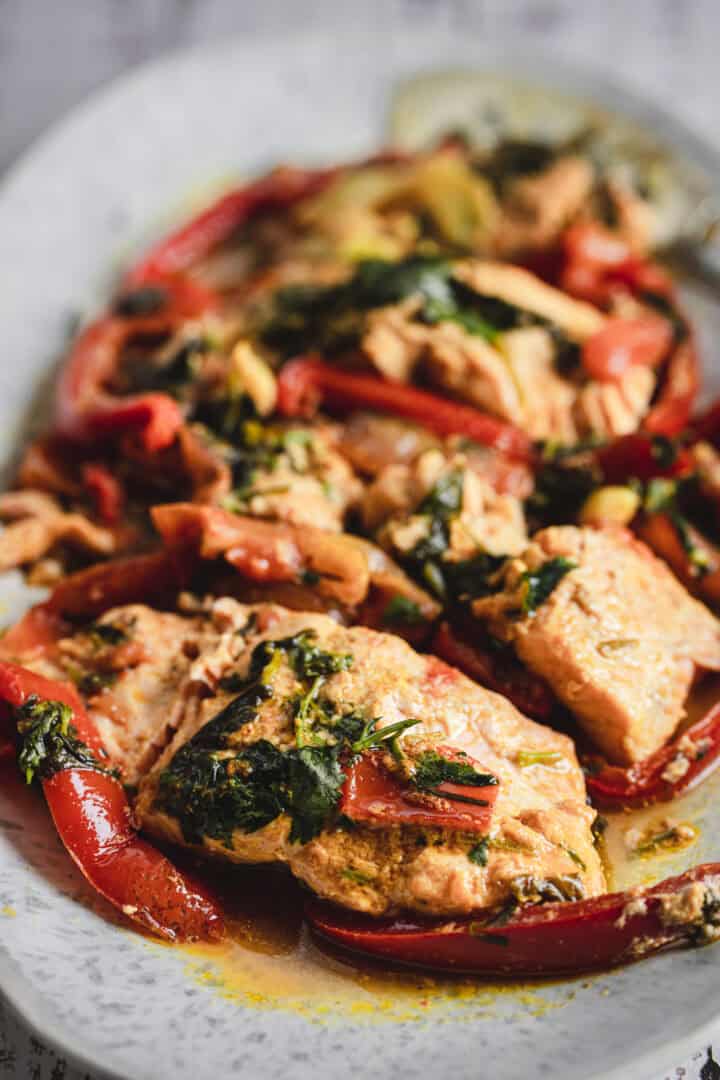 Moroccan salmon fillets with red bell peppers and greens in a flavorful sauce, served on a white plate.