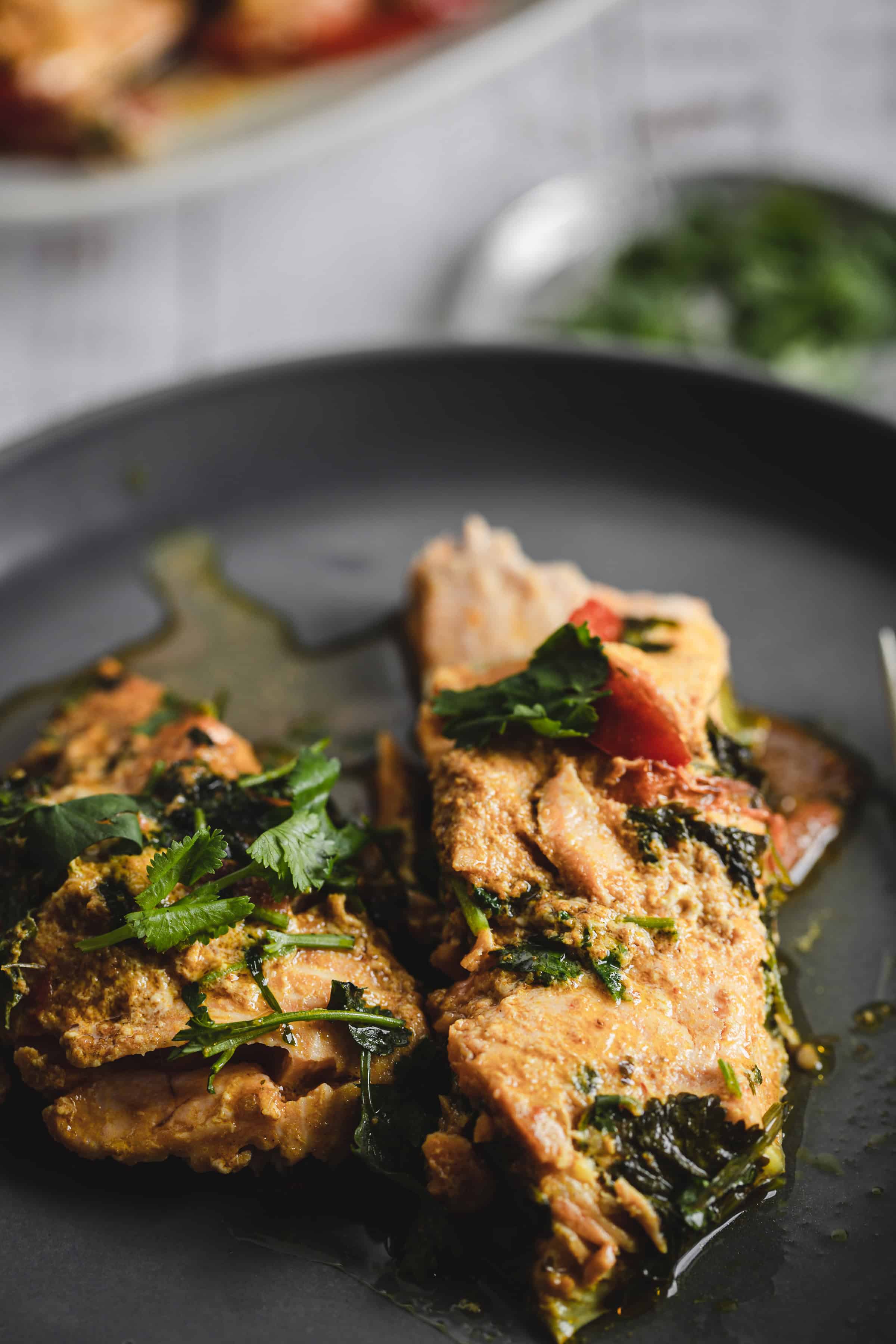 Moroccan salmon cooked to perfection, garnished with fresh cilantro and sauce, served on a dark plate.