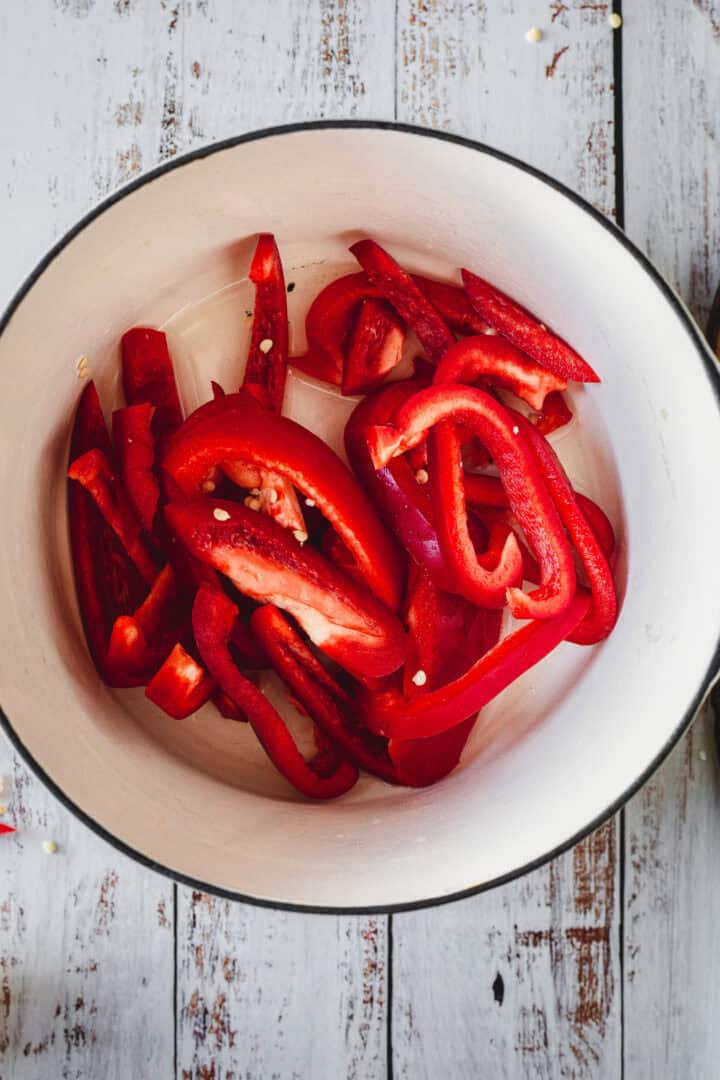 Sliced red bell peppers in a white pot on a rustic wooden surface, perfect for pairing with Moroccan salmon.