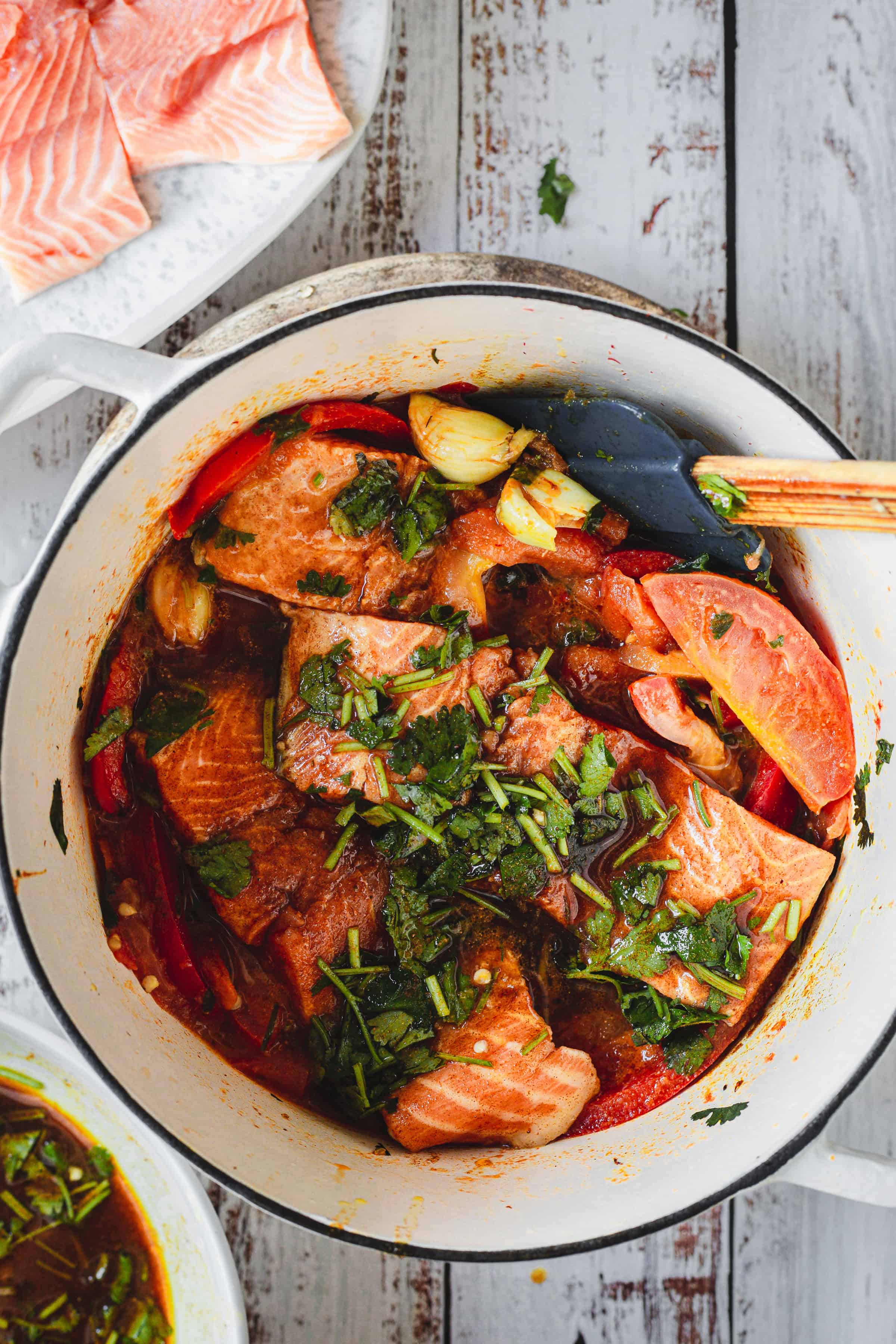 Chunks of Moroccan salmon, herbs, and vegetables simmering in a pot with a savory broth, ready to cook.