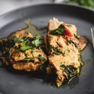 Two pieces of saucy Moroccan salmon, garnished with fresh herbs, rest on a dark plate.