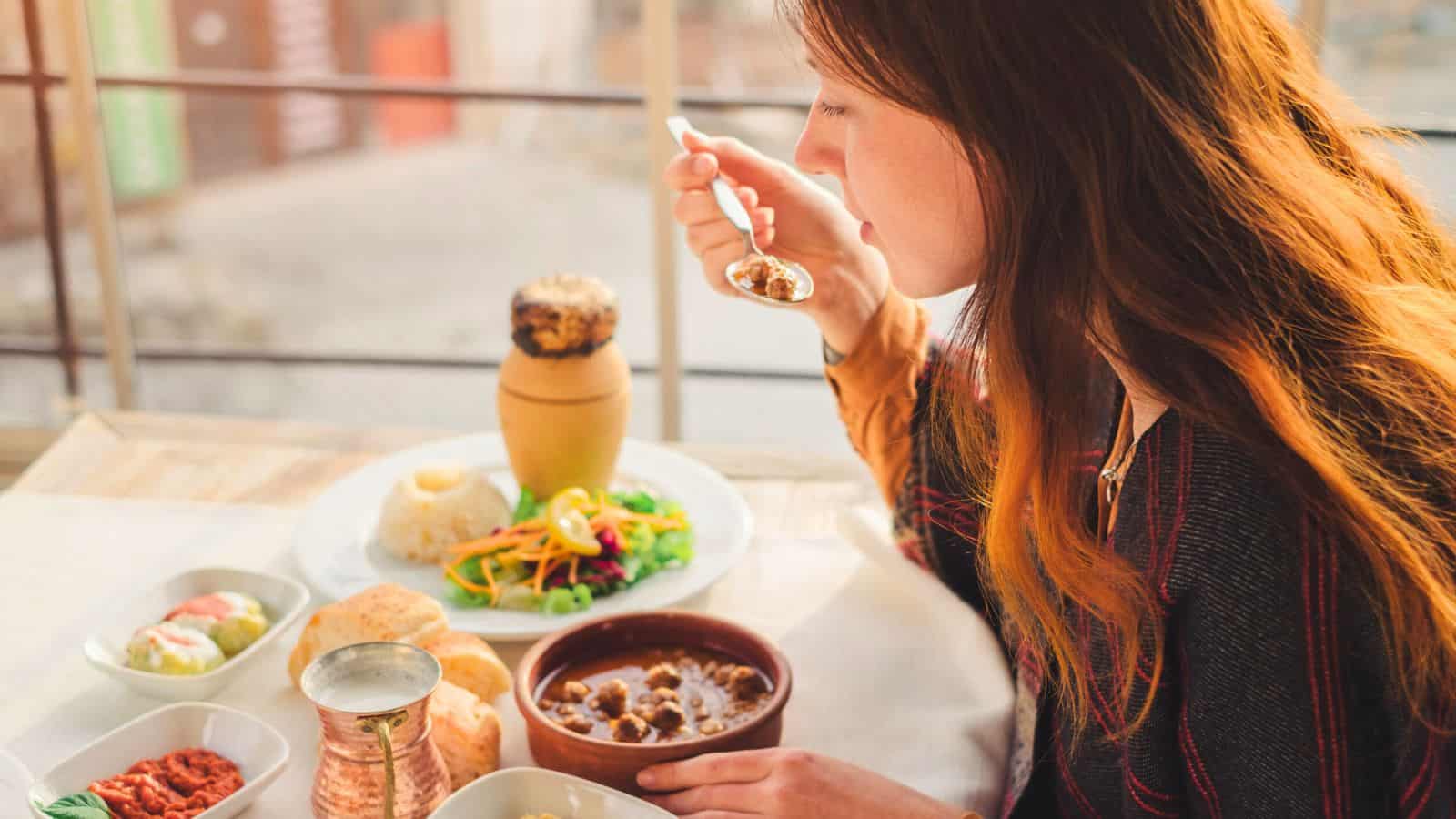 A woman enjoys a meal at a table with soup, bread, rice, and salad, observing global food etiquette rules as she samples each dish.