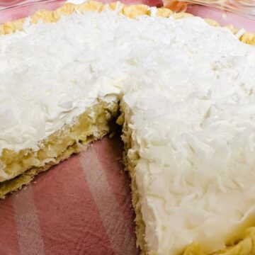 A coconut cream pie with a slice missing, showing creamy filling and topped with shredded coconut.
