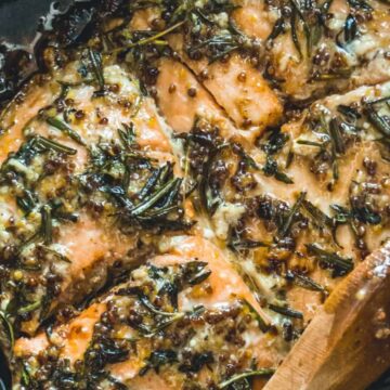 Salmon fillets cooked with herbs and spices in a pan, being stirred with a wooden spoon.