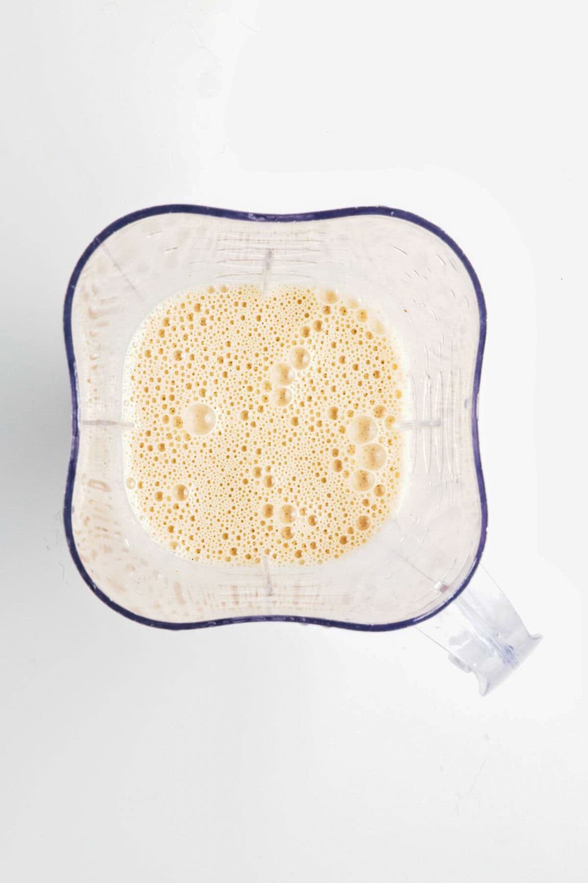 Top view of a blender with a frothy light orange liquid inside, perfect for pairing with Peanut Butter Banana Overnight Chia Oats, set against a white background.