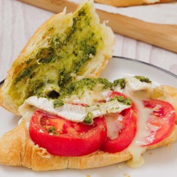 Enjoy a delicious Pesto Tomato Brie Croissant Sandwich, featuring tomato slices, melted brie cheese, and green pesto inside a flaky croissant on a plate.