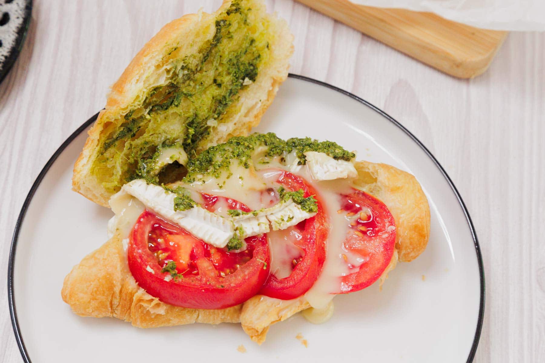 A Pesto Tomato Brie Croissant Sandwich with melted cheese, served on a white plate.