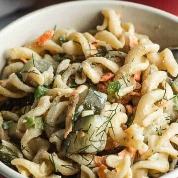 A bowl of rotini pasta salad with cucumbers, carrots, and herbs, with a fork inside.