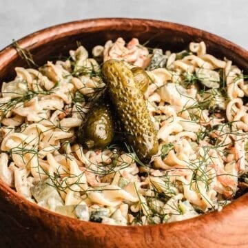 Pickle Pasta Salad with fresh herbs, crisp vegetables, and three pickles on top, served in a rustic wooden bowl.