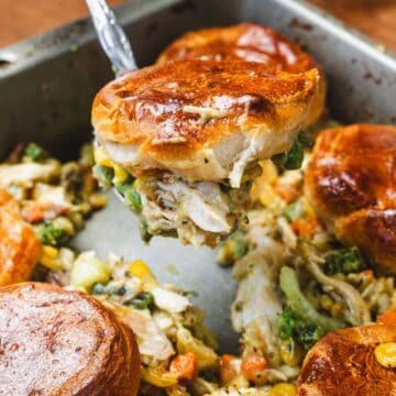Golden biscuit-topped chicken pot pie with vegetables being served from a baking pan.