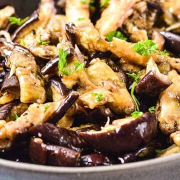 A bowl of cooked eggplant slices garnished with fresh parsley—perfect as light and flavorful Labor Day appetizers.