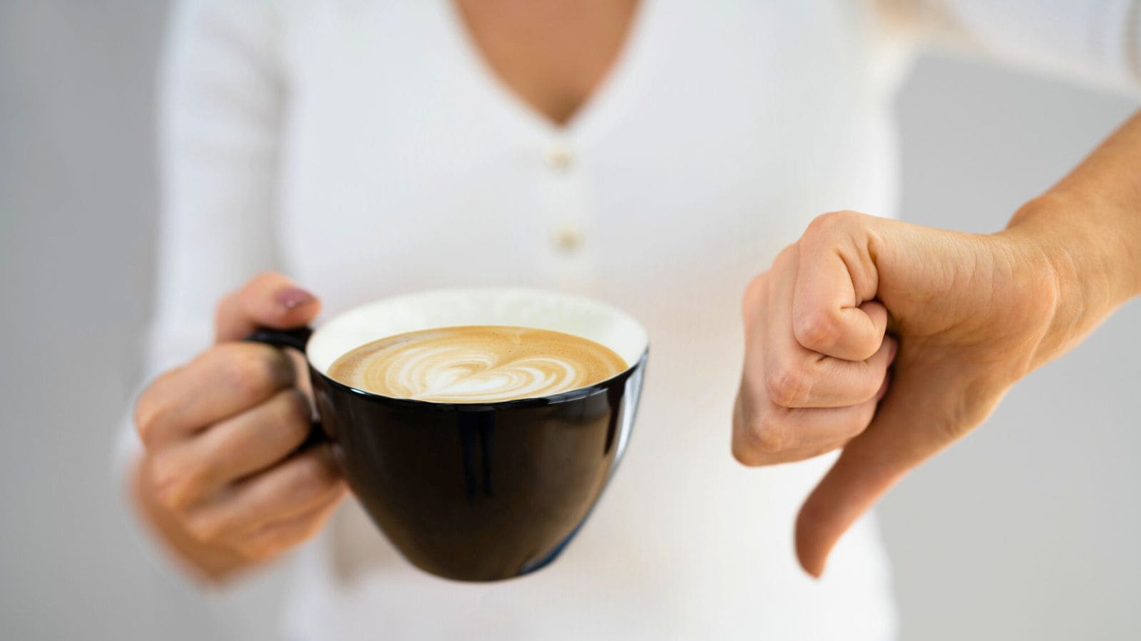 Person holding a cup of coffee in one hand and showing a thumbs-down gesture with the other hand.