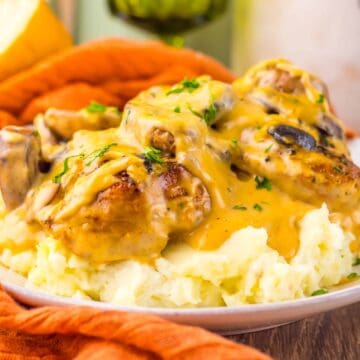 Mashed potatoes topped with chicken, mushrooms, and creamy gravy on a white plate.