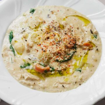 Creamy soup with vegetables and herbs in a white bowl, next to a spoon and a striped towel.
